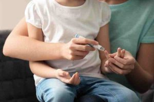 A mother collecting a blood sample from her diabetic daughter with a lancet pen at home.