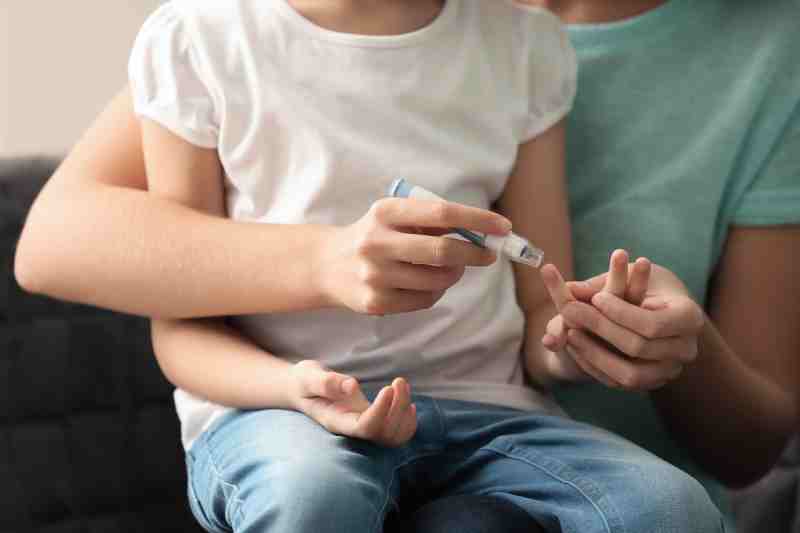 A mother collecting a blood sample from her diabetic daughter with a lancet pen at home.
