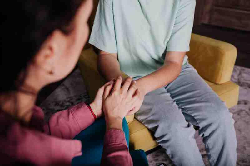 Two people sitting closely, holding hands in a caring conversation about struggles and challenges.