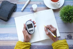 An old people recording glucose levels after using a glucometer at home.