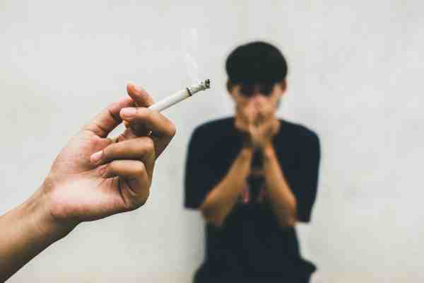 A man covering his face from smoke, symbolizing the importance of quitting smoking to prevent pre-diabetes.