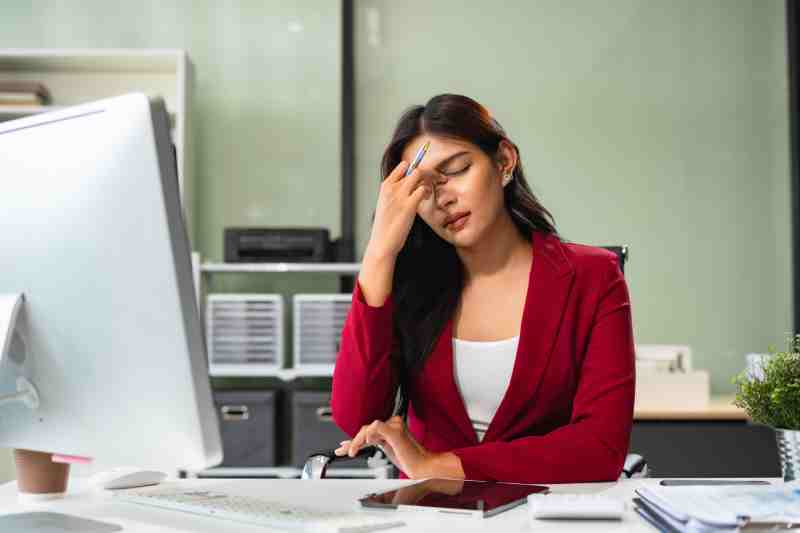 A woman holding her head at work, illustrating that stress can be a contributing factor to diabetes.