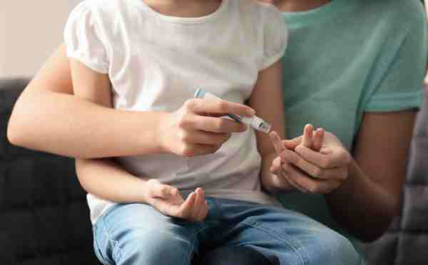 A woman using a lancet pen to check her daughter’s insulin levels for type 1 diabetes management.