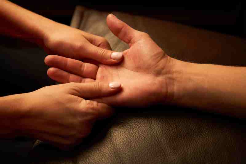 Therapist's hands applying acupressure to a client's palm as part of traditional Chinese medicine.