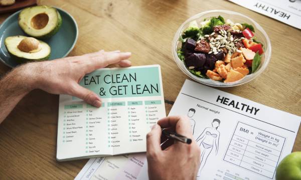 Person planning a healthy diet with a salad, clean eating guide, and BMI chart, representing a personalized approach for a woman with diabetes.