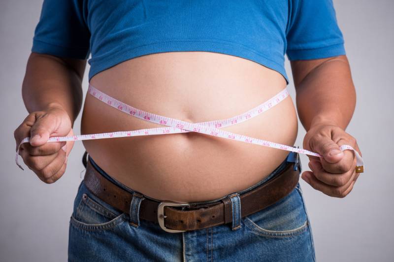 An overweight person measuring their waist, showing health risks like type 2 diabetes and heart disease.