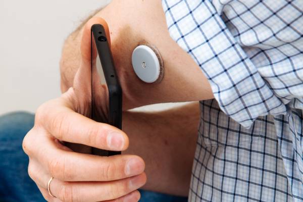 A person using a CGM device, representing the role of modern tools like CGMs and insulin pumps in diabetes management.
