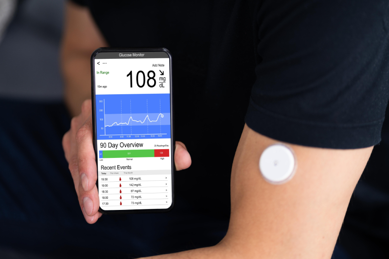 A person using a continuous glucose monitor and app for blood sugar testing in diabetes management.