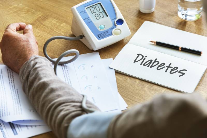 A man checks his blood pressure beside medical documents labeled 'Diabetes,' reflecting advances in diabetes care.