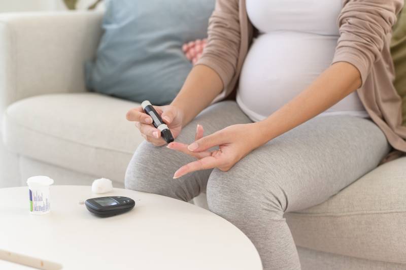 Pregnant woman using a digital glucose meter to check blood sugar, illustrating gestational diabetes.