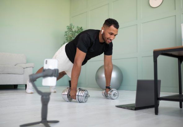A man working out with dumbbells at home while watching a fitness video, symbolizing how exercise supports blood sugar management.