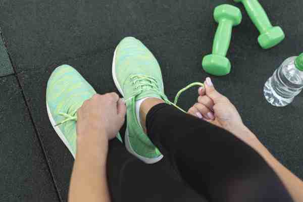 A person with diabetes tying shoelaces near a dumbbell, symbolizing the need for medical and risk assessments before exercising.
