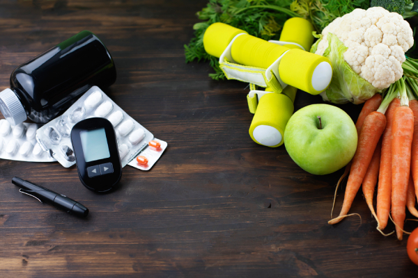Glucose meter, medications, dumbbells, and healthy foods illustrating the role of diet and exercise in managing diabetes.