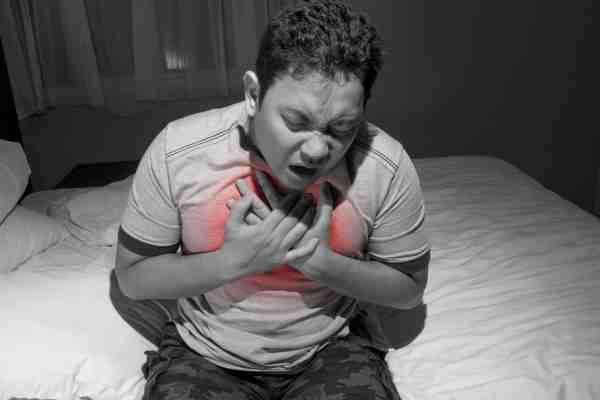 Man lying awake in bed at night, clutching his chest, showing possible signs of a heart attack.