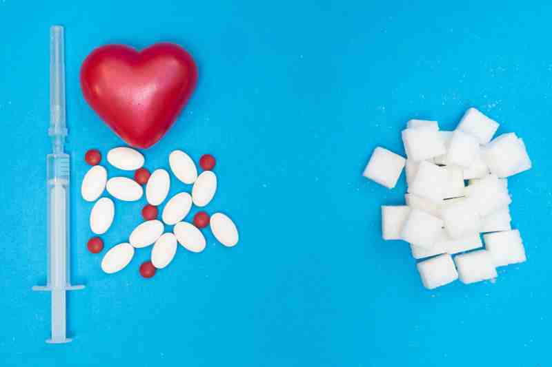 Medication, a heart model, insulin, and sugar cubes representing the link between diabetes and early heart disease.