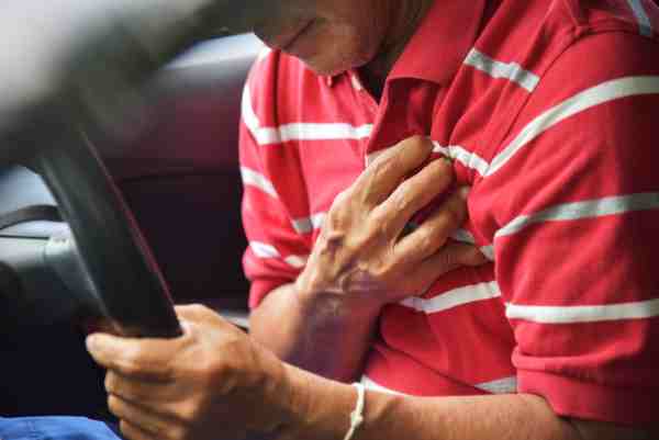 Elderly man clutching his chest in pain while driving, illustrating the danger of having a heart attack.