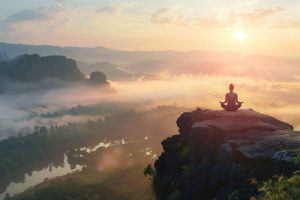 Person meditating on a cliff at sunrise, symbolizing stress management.