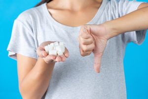 A woman holding sugar cubes with a thumbs-down gesture, symbolizing a rejection of sugar.