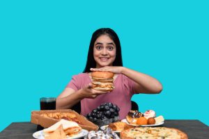A girl overeating, surrounded by various food items on the table, representing a symptom of diabetes.