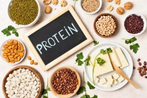 The word 'Protein' written on a slate, accompanied by nuts, milk products, and pulses, representing the role of protein and fat in diabetes management.