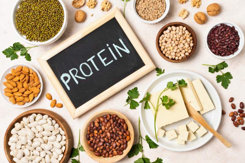 The word 'Protein' written on a slate, accompanied by nuts, milk products, and pulses, representing the role of protein and fat in diabetes management.