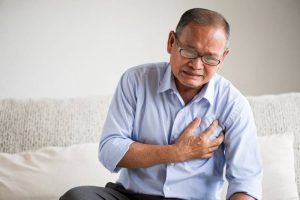 Senior man clutching his chest in pain, indicating a heart attack caused by lack of oxygen to the heart muscle.