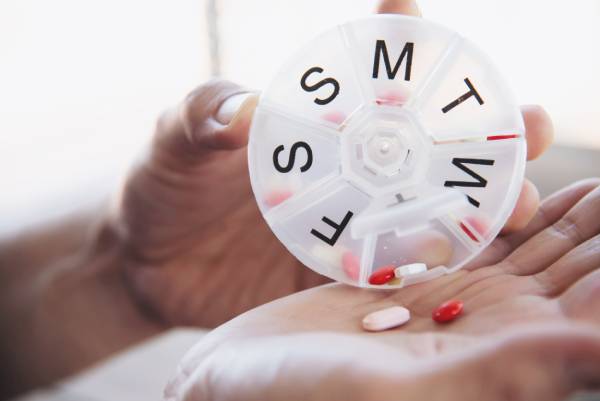 Person taking pills from a weekly planner as a medication reminder.