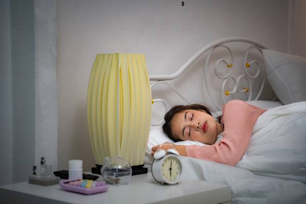 A young girl with diabetes sleeping in bed, with an alarm set, symbolizing the importance of rest for proper body function