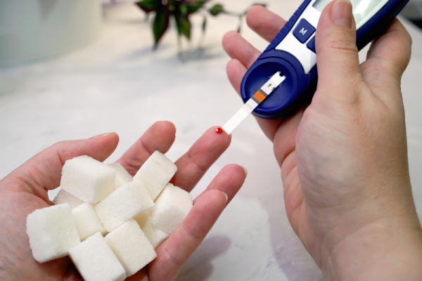 A person checks blood with a glucometer beside a hand holding sugar, symbolizing diabetes.