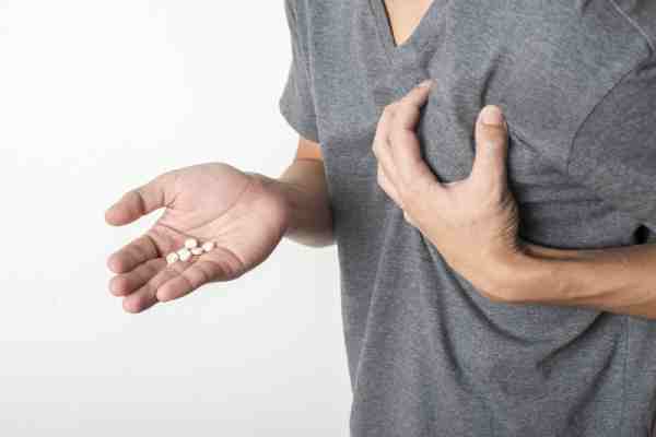 Man holding his chest in pain with pills in his other hand, indicating signs of a heart attack.