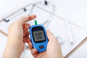 A person checking a blood sample with a glucometer, surrounded by a stethoscope, represents a test for Type 1 diabetes.
