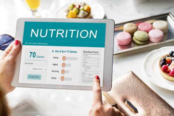 Woman holding a tablet with nutrition and calorie info beside a meal on the table.