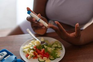 Woman checking her glucose level next to a salad on the table.