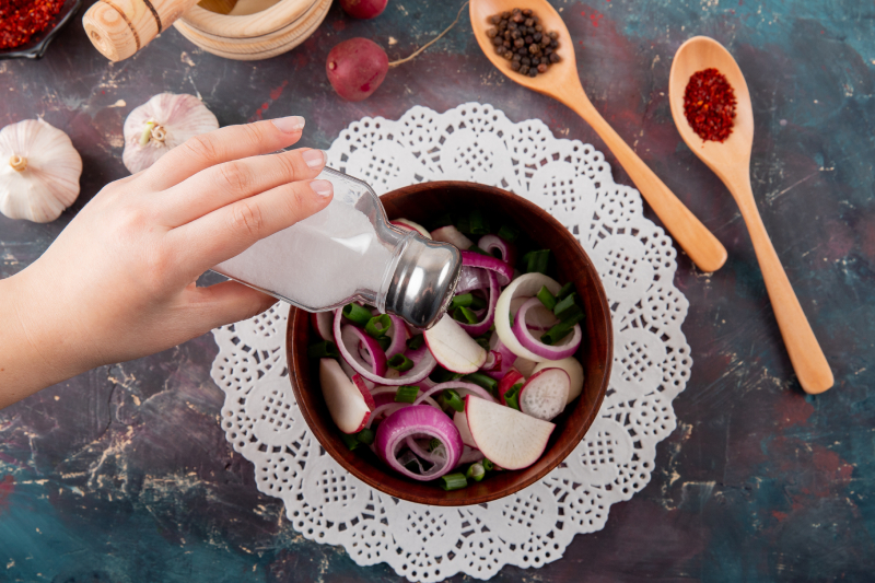 A person sprinkles extra salt on salad, representing a diet high in sodium that may lead to hypertension.