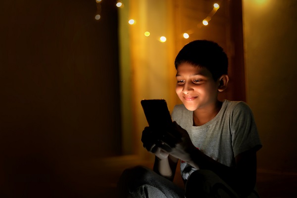 Smiling boy using a smartphone in a dark room, suggesting screen time awareness.