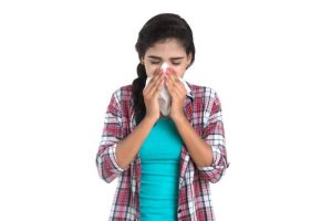A young girl covering her nose with a handkerchief and eyes shut, indicating cold symptoms.