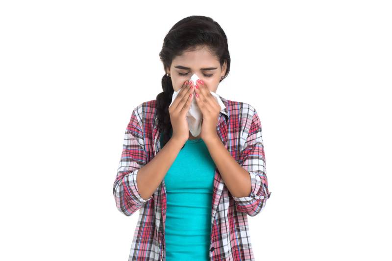 A young girl covering her nose with a handkerchief and eyes shut, indicating cold symptoms.