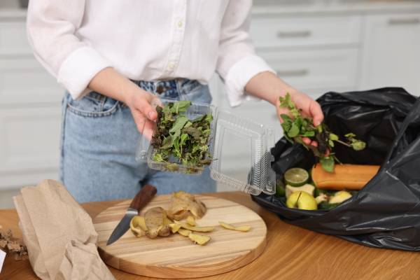 Woman disposing food scraps in trash, stressing waste must be cleared immediately to avoid odors and pests.