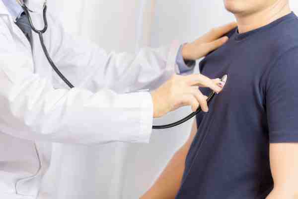 Doctor checking young man with stethoscope, stressing the importance of recognizing silent heart attack signs.