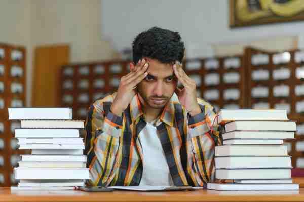 Stressed male student sitting at a library desk, showing signs of a silent heart attack at age 30