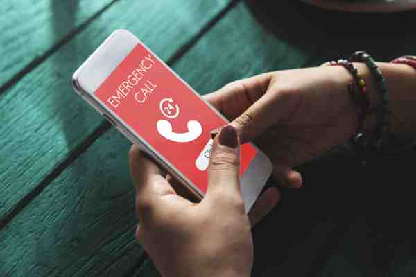 Woman suffering a heart attack alone, using a smartphone that displays 'EMERGENCY CALL' on the screen.