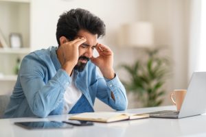 A stressed man holding his head in a work setting, showing early signs of high blood pressure.