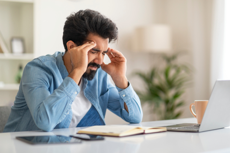 A stressed man holding his head in a work setting, showing early signs of high blood pressure.