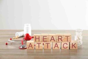 Wooden blocks spelling 'HEART ATTACK' with stethoscope, pill bottles, and red heart on a desk.