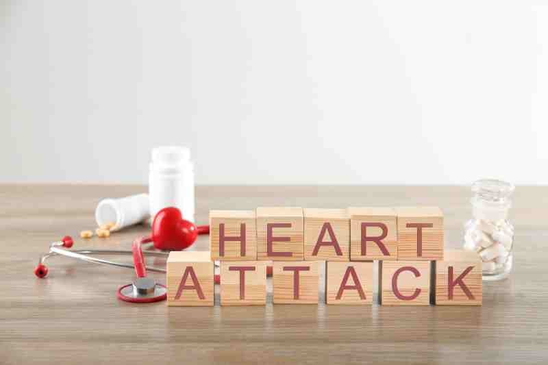Wooden blocks spelling 'HEART ATTACK' with stethoscope, pill bottles, and red heart on a desk.