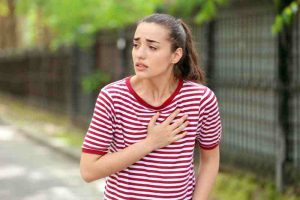 Woman clutching her chest in pain outdoors, indicating early warning signs of a heart attack.