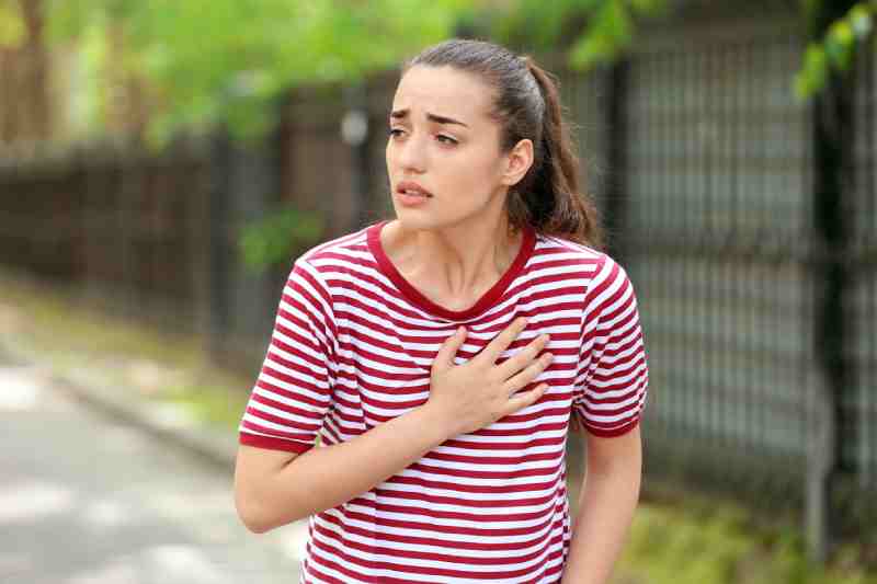 Woman clutching her chest in pain outdoors, indicating early warning signs of a heart attack.