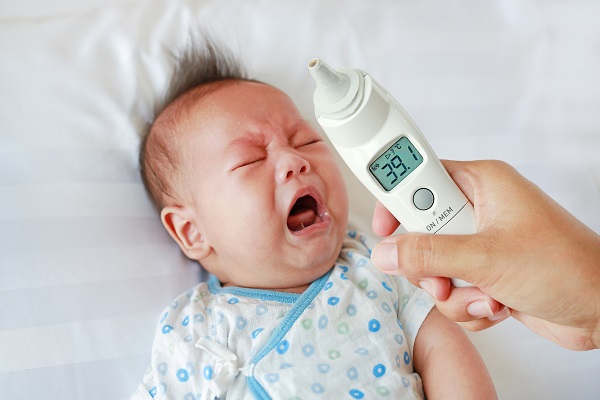 A person is checking a crying 3-month-old baby's temperature with a thermometer, indicating a high fever.