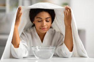A woman inhaling steam from a bowl with her head covered by a towel, a common home remedy for cold and cough.
