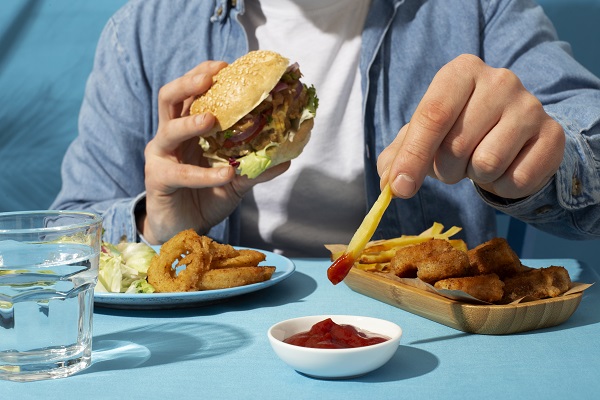 A person holding a burger alongside other fast food represents poor diet choices associated with high blood pressure.